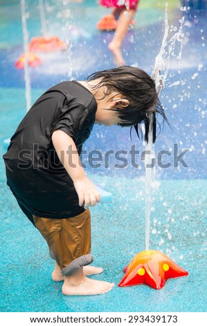 Happy asian boy has fun playing in water fountains in water park