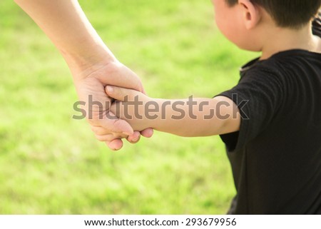 Hands of mother and son holding each other. Summer park in background