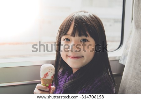 Little asian girl smiling  and eating ice cream.She travels on a train,vintage filter