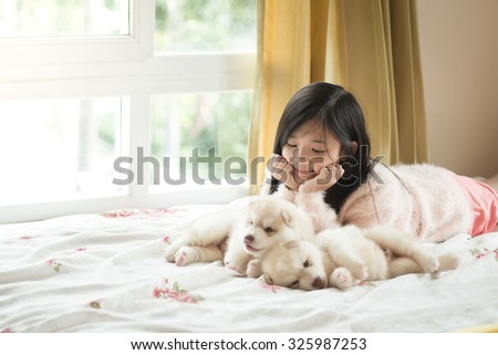 Little asian girl lying with two siberian husky puppies on bed