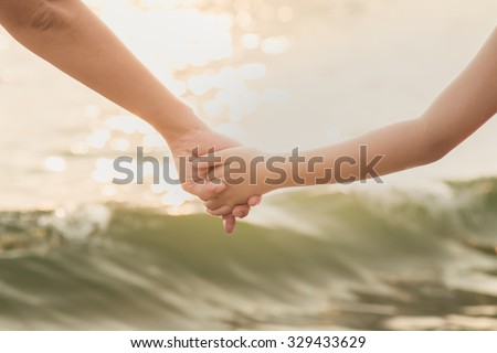 Hands of mother and daughter holding each other on sea background