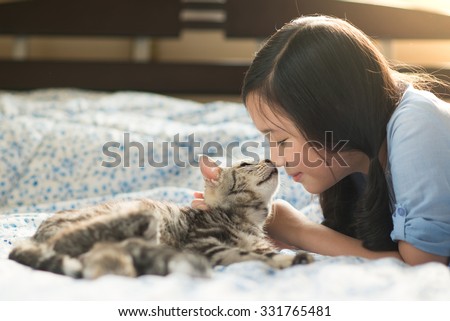 Beautiful asian girl kissing american shorthair cat on the bed