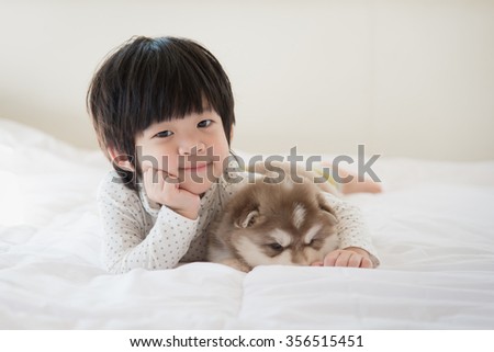 Cute asian child and siberian husky puppy lying on white bed