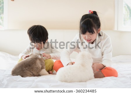 Little asian children kissing puppy on white bed