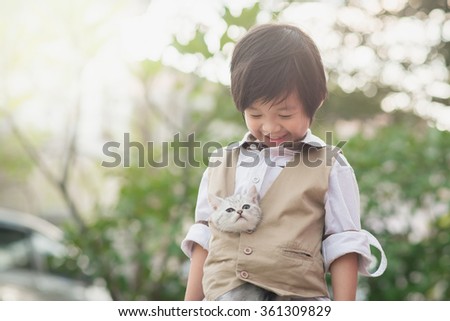 Cute Asian boy holding american short hair  kitten with sunshine in the park, vintage filter