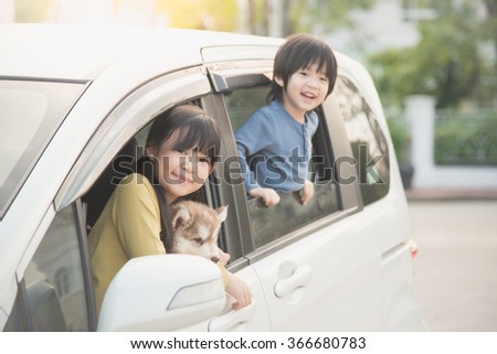 Happy asian children and siberian husky puppy sitting in the car