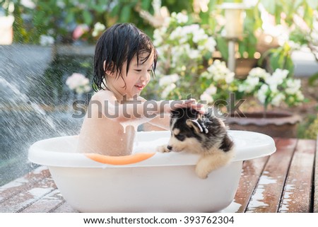 Cute asian  child bathing with siberian husky puppy in the garden on a hot sunny summer day