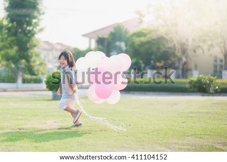 Cute Asian child with many balloons playing in the park under sunlight on summer day