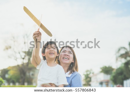 Cute Asian mother and son playing cardboard airplane together in the park outdoors