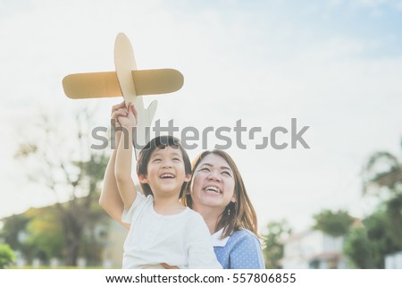 Cute Asian mother and son playing cardboard airplane together in the park outdoors