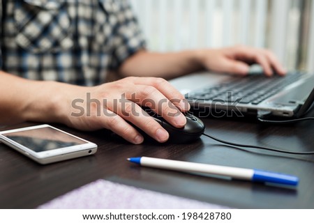 Hands of white man holding a mouse and printing on a keyboard