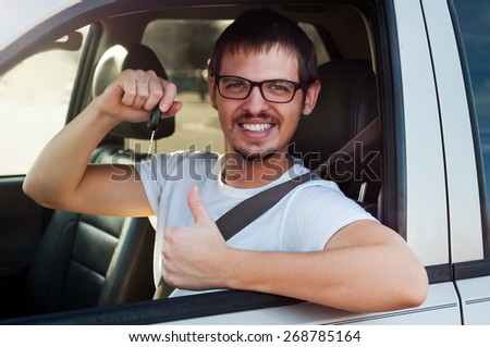 Young male european driver is holding new car key and showing thumb up