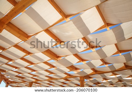 Canvas roof stretched over wooden structure on outdoor patio in a sunny day.