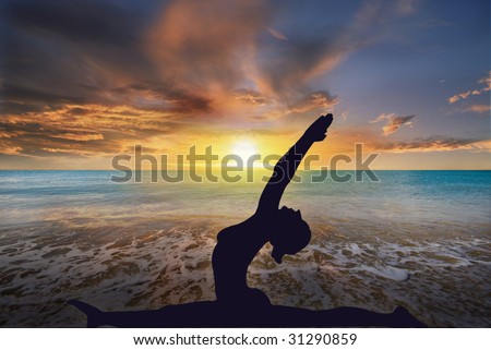 Young woman doing yoga exercise as the sun sets over the ocean