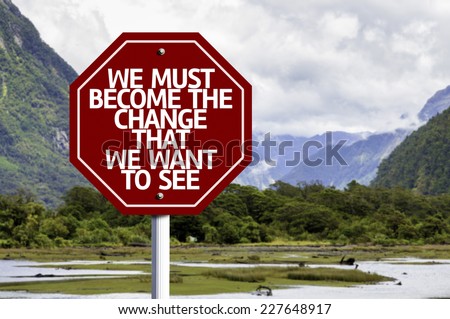 We Must Become The Change That We Want to See written on red road sign with landscape background