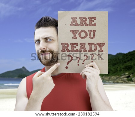 Man holding a card with the text Are you Ready? on a beach background