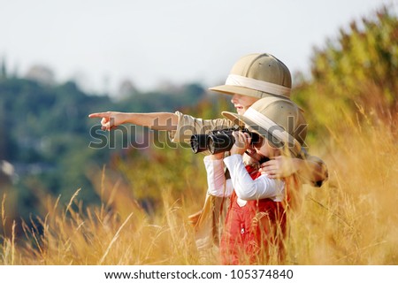 Happy young safari adventure children playing outdoors in the grass with binoculars and exploring together as brother and sister.