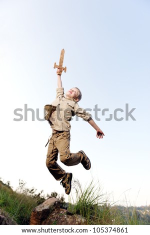 Young boy jumping with wooden sword playing an adventure exploring game outside
