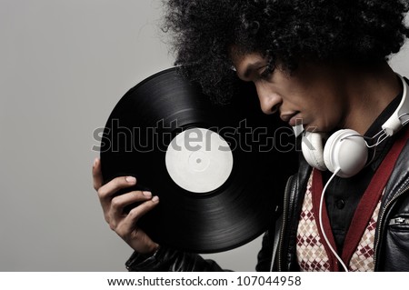 Retro dj portrait in fashion style isolated on grey background in studio. Modern music man with afro hairstyle, headphones and vinyl record.