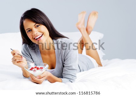 morning breakfast meal woman eating healthy yoghurt and fruit in bed while happy and smiling isolated on grey background