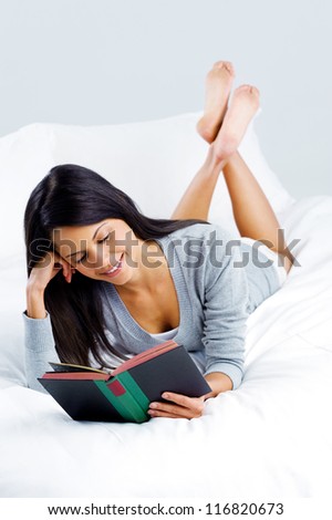 leisure reading woman is comfortable lying on her bed with a book, smiling and happy isolated on grey background