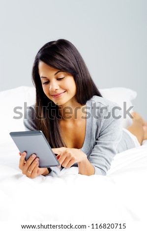woman reading with modern digital tablet device while lying on bed isolated on grey background
