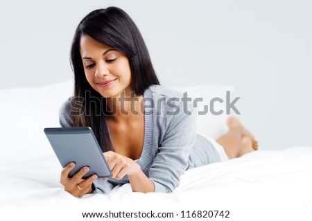 woman reading with modern digital tablet device while lying on bed isolated on grey background