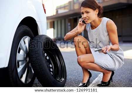 Woman calling for assistance with flat tire on car in the city