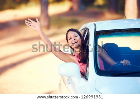 Happy woman waving from drivers seat in car while traveling
