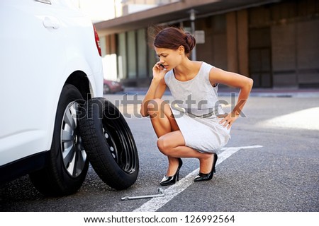 Woman calling for assistance with flat tire on car in the city