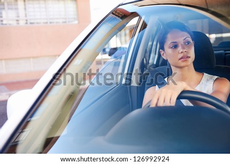 successful businesswoman driving car through modern urban city with reflections of buildings