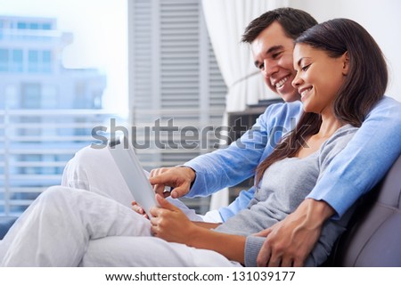 couple relaxing at home with tablet computers reading in the living room on the sofa couch.