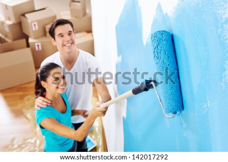 overhead view of couple having fun renovating their new home together with blue paint on a roller