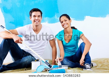 cute couple painting new home together portrait while sitting on wooden floor