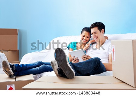 couple moving in together relaxing on sofa couch with laptop tablet computer and boxes
