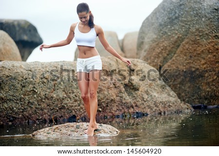 Woman on rock at beach dipping toes in water, having fun outdoor lifestyle