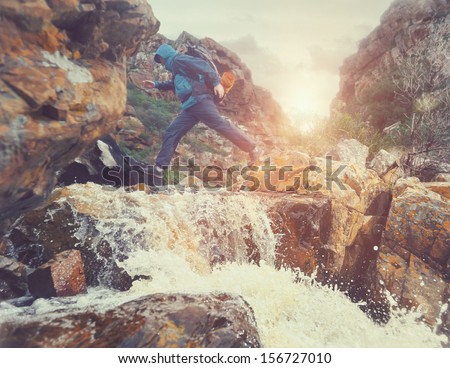 Survival man crossing river in mountains with backpack, sunrise or sunset and danger