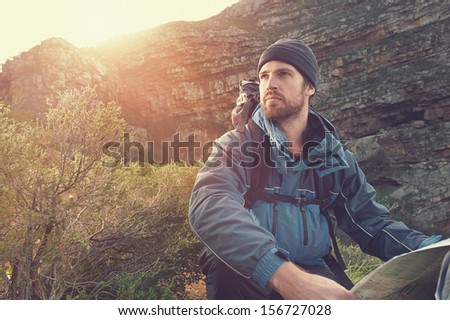 portrait of adventure man with map and extreme explorer gear on mountain with sunrise or sunset