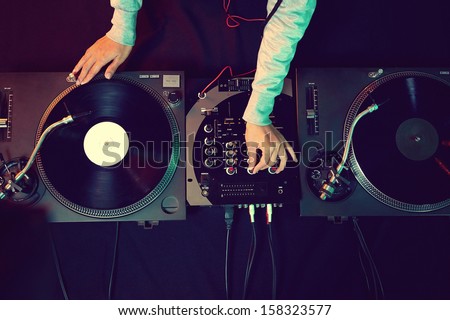 Dj hands on equipment deck and mixer with vinyl record at party
