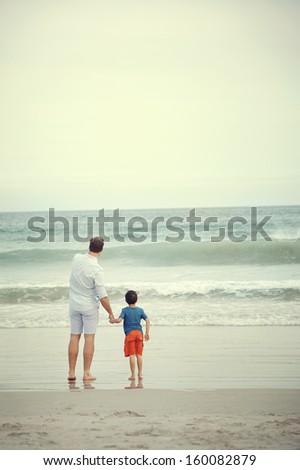 Father And Son At Beach Holding Hands Looking At The Ocean Together On Vacation
