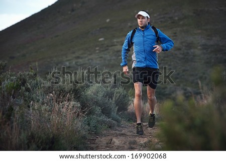 ultra marathon trail runner training in mountains for fitness and exercise wearing windbreaker