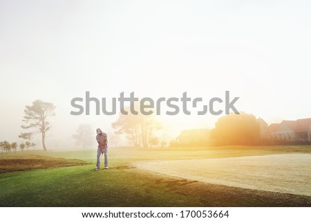 Golfer chipping onto the green at sunrise on the golf course in misty conditions