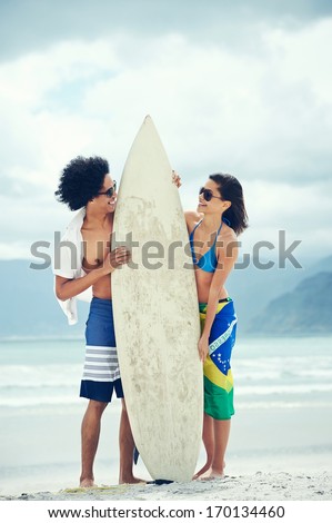 Couple having fun together at the beach with surfboard and brasil flag