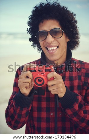 Happy hipster man smiling with toy camera at the beach