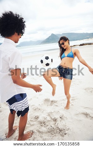 Latino Couple Playing Soccer On Beach With Ball Kicking And Having Fun