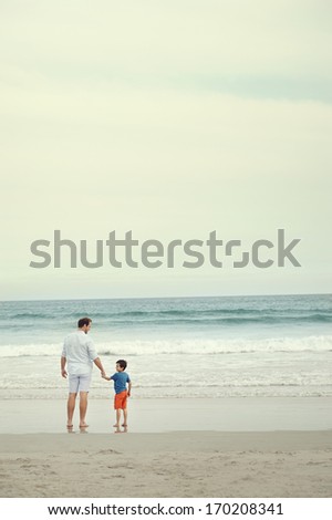 Father and son at beach holding hands looking at the ocean together on vacation