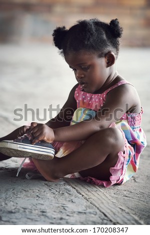 Young african girl tying shoelace and putting shoot on foot in rural setting
