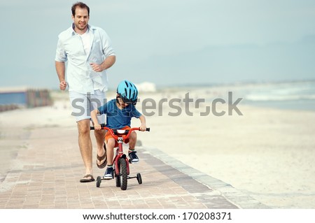 Father and son learning to ride a bicycle at the beach having fun together