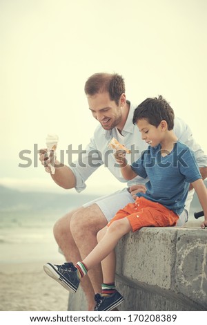 Father and son eating ice-cream together at the beach on vacation having fun with melting mess