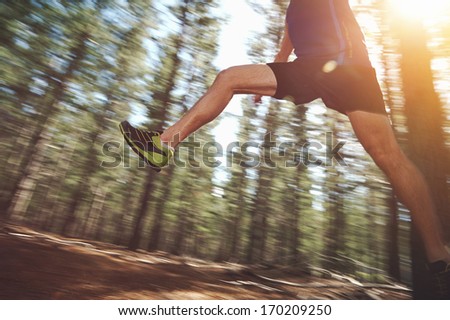 Runner jumping on trail run in forest for marathon fitness